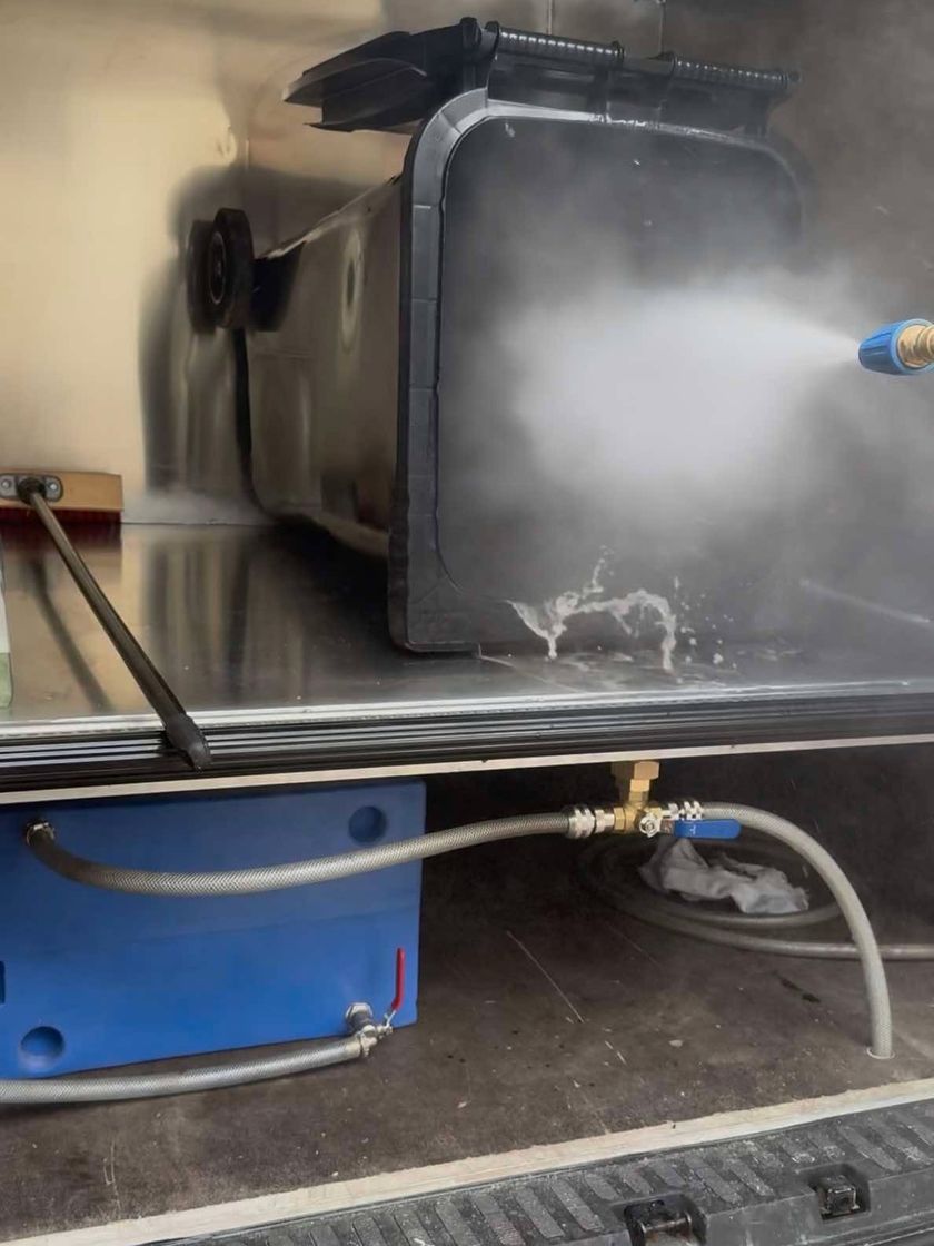 Un conteneur poubelle noir lavé au jet haute pression dans le caisson inox du camion